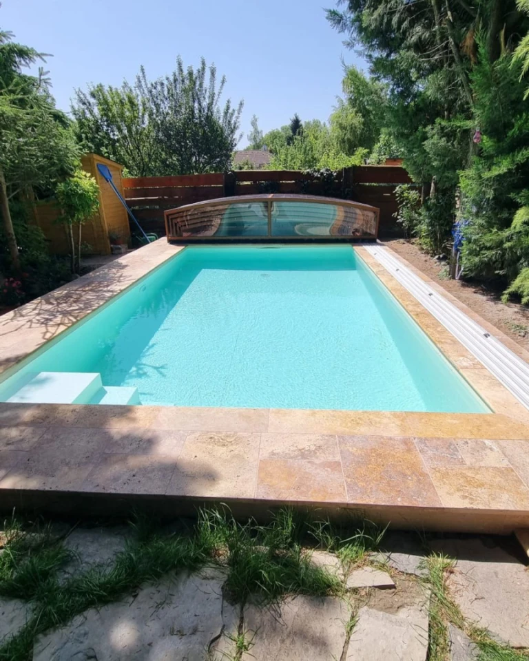 A modern pool with clear turquoise water and a low-profile sliding roof in the garden.