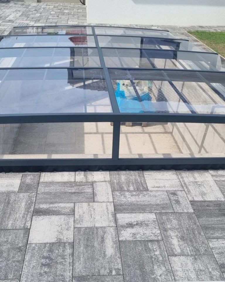 Modern low-profile pool enclosure with an anthracite frame and clear polycarbonate panels