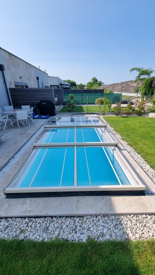 A modern, low-profile pool enclosure with a transparent panel in the garden of a single-family home.