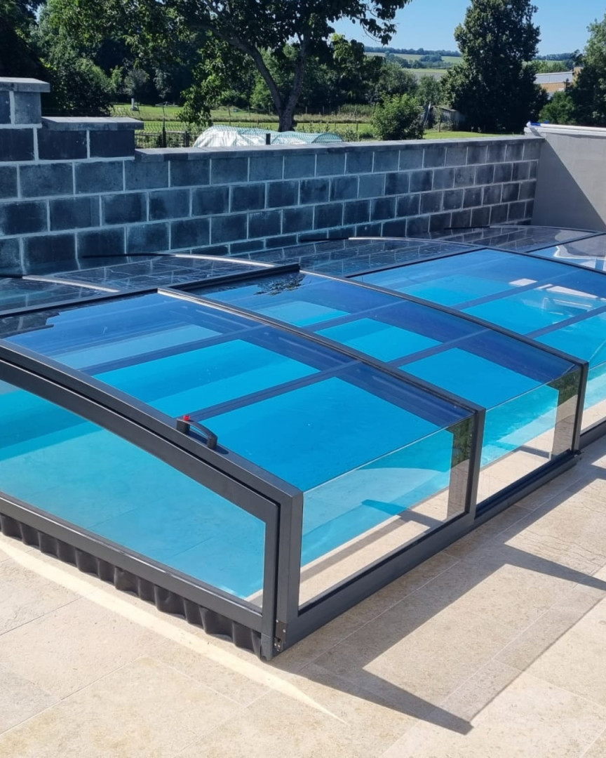 A modern, low-profile pool enclosure with clear panels in the garden