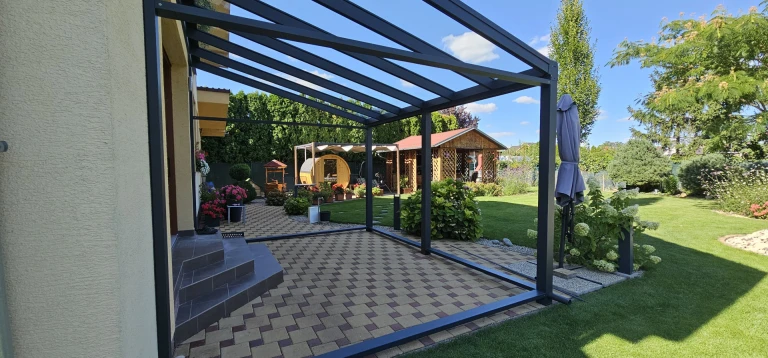 A modern anthracite-colored aluminum patio structure with a translucent roof in a well-maintained garden