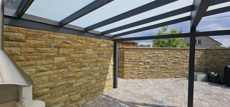A modern aluminum conservatory structure with a glass roof next to a stone wall