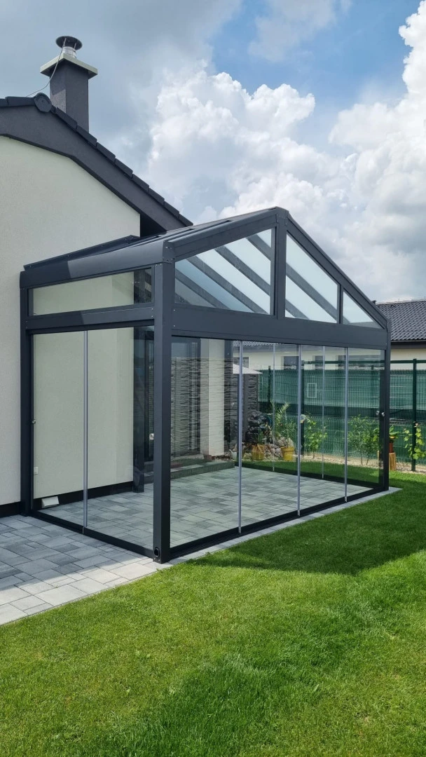 A modern, glass-enclosed sunroom with an anthracite-colored aluminum frame attached to a single-family home