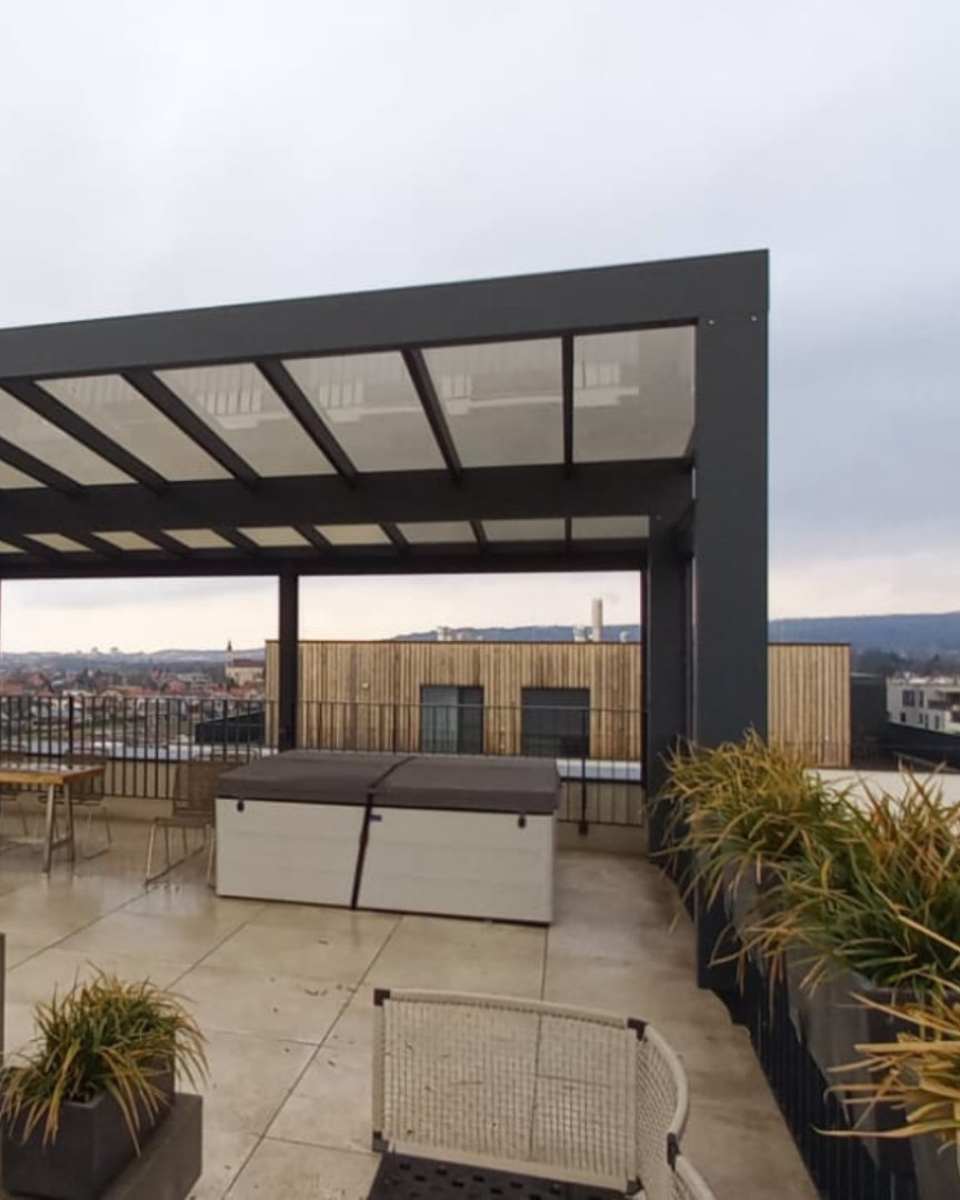 A modern aluminum pergola on a rooftop terrace with a view of the city and a hot tub