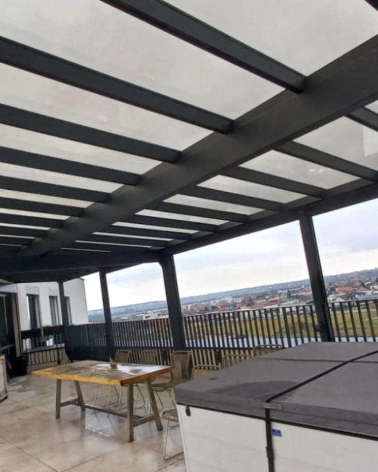 A modern glass-enclosed aluminum pergola on the terrace overlooking the city, with a table and chairs