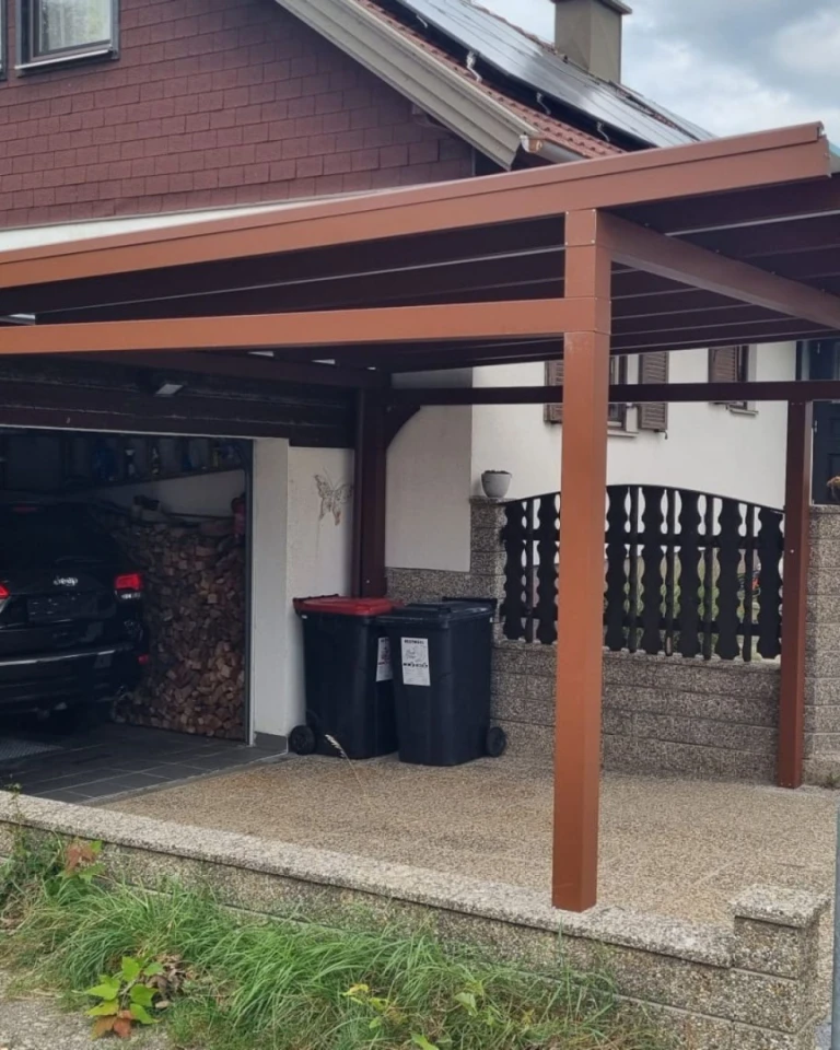 A brown carport next to a single-family home with a garage and trash cans
