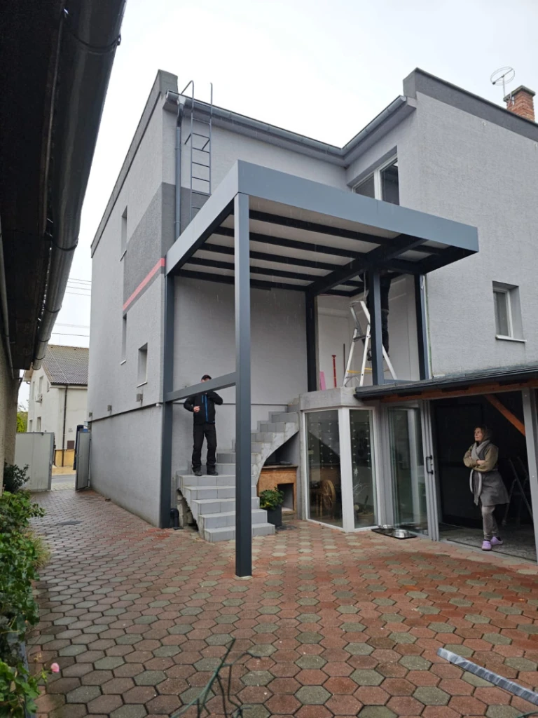 A modern gray aluminum pergola installed above the staircase of a single-family home