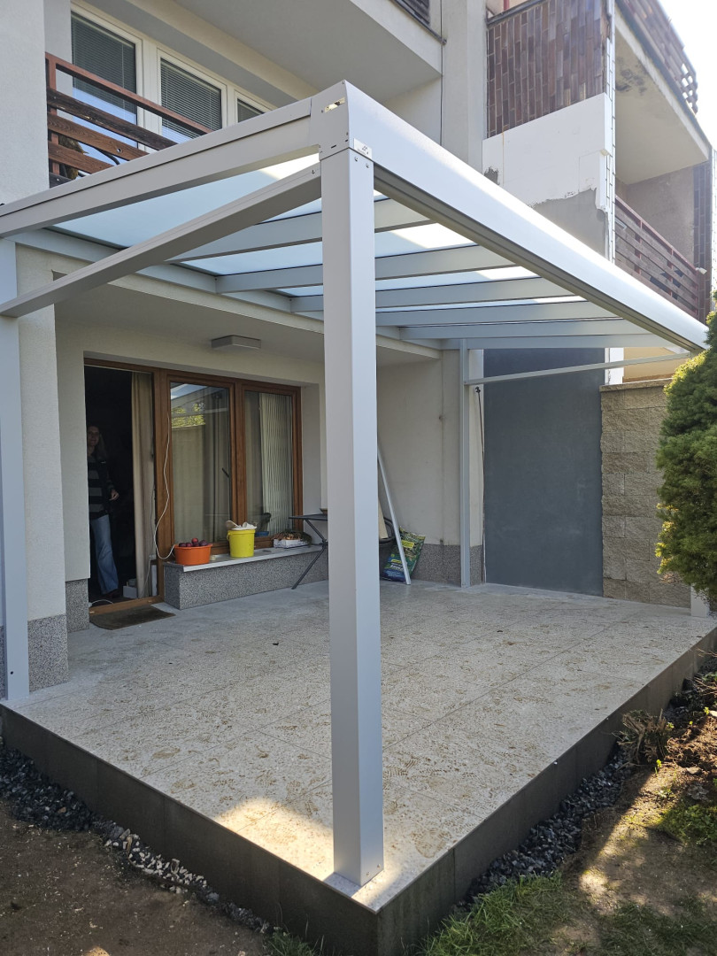 A modern aluminum pergola with a glass roof on the terrace of a single-family home