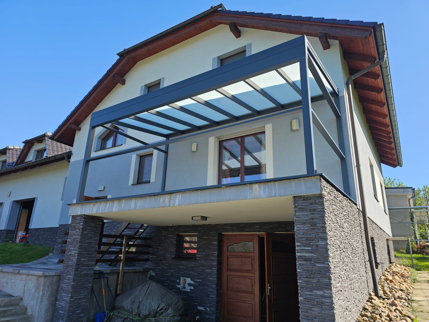 A modern aluminum pergola with a glass roof installed on the balcony of a single-family home