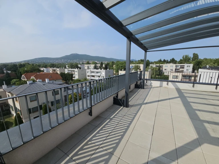 A modern aluminum pergola with a glass roof on a spacious terrace overlooking the city and the mountains.