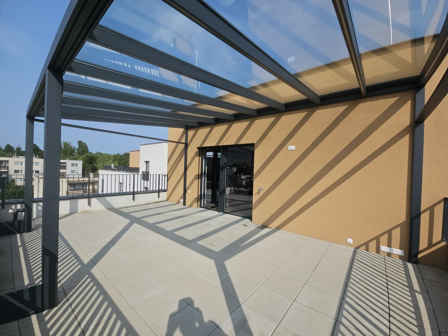 A modern aluminum pergola with a glass roof on the terrace of an apartment building