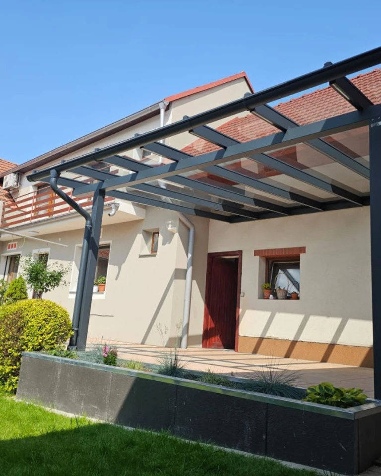 A modern anthracite-colored aluminum pergola with a glass roof attached to a single-family home