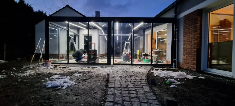 An evening view of the installation of a glass-and-aluminum pergola with integrated LED lighting at a single-family home.