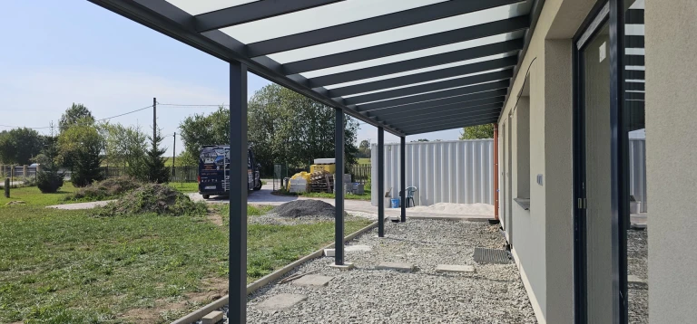 Side view of the ROBUST aluminum pergola with a glass roof installed next to a single-family home