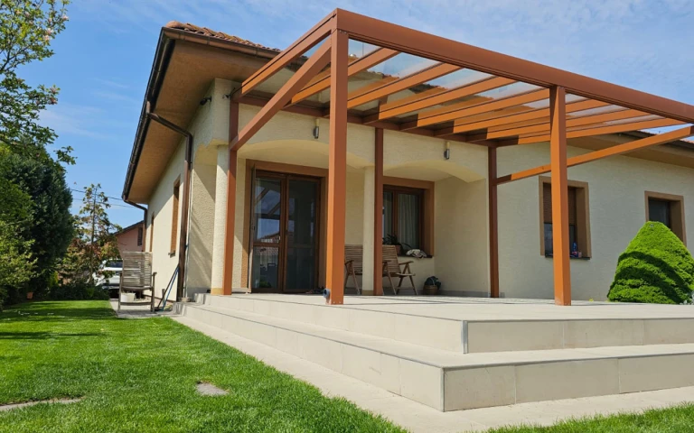 A brown aluminum pergola with a glass roof installed on the patio of a single-family home