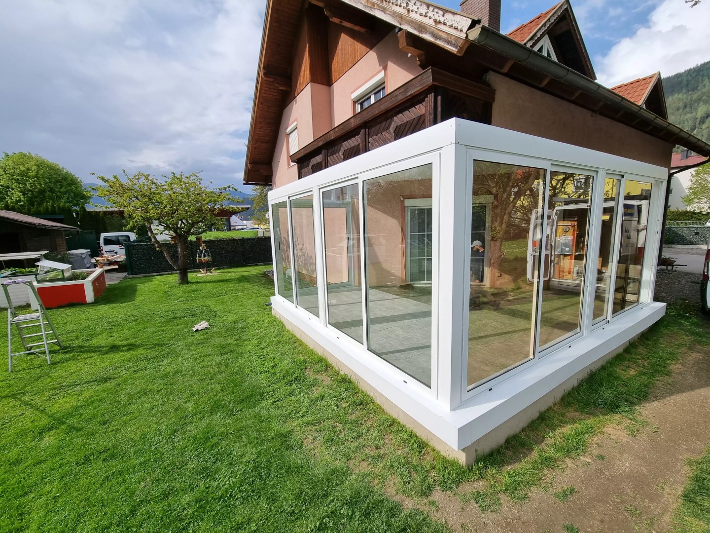 A modern white, glass-enclosed aluminum pergola in the garden of a single-family home.