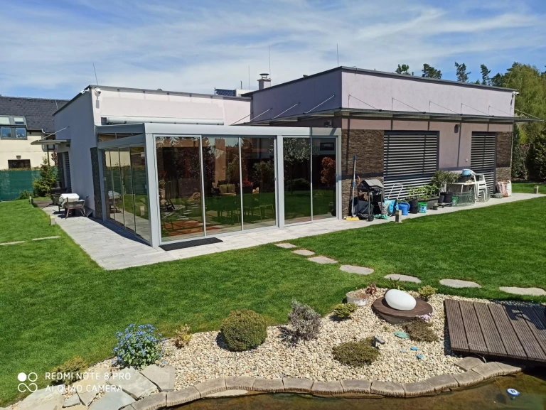 A modern aluminum pergola with glass panels in the garden of a single-family home
