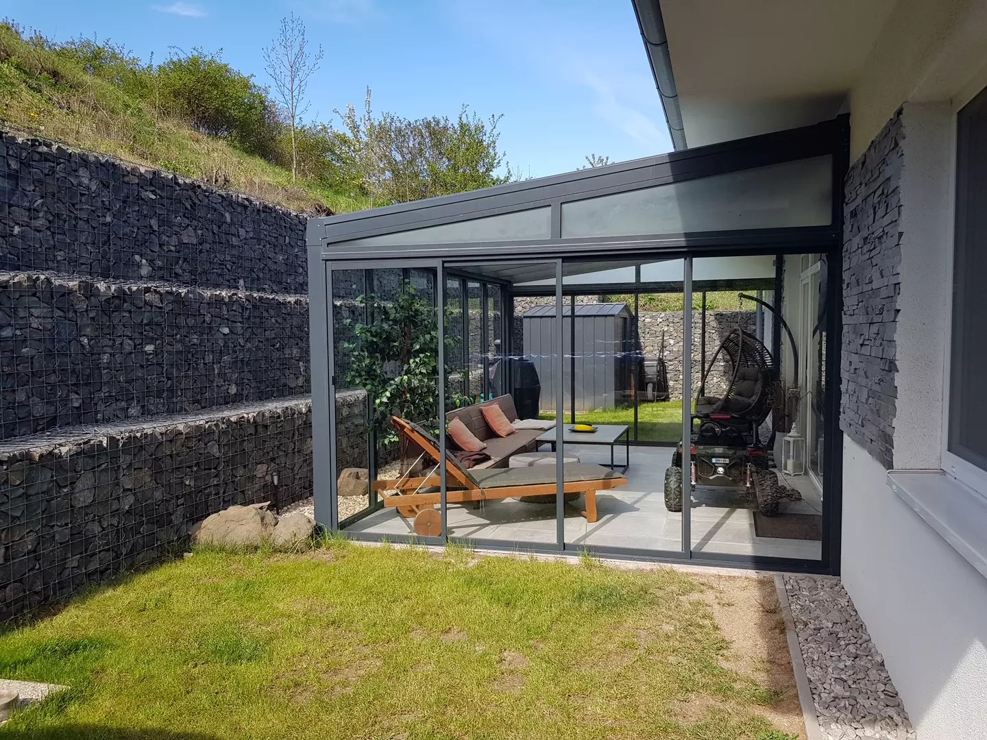 A modern aluminum pergola with a glass roof and a sliding system next to a house in Braňany.
