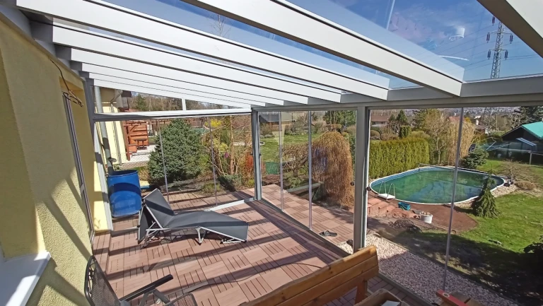 A modern, glass-enclosed aluminum pergola with a patio and a view of the garden and pool