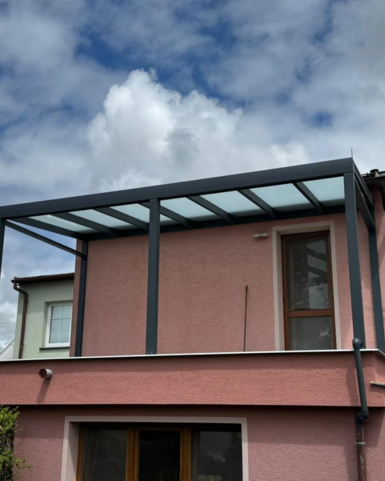 A modern dark gray aluminum pergola with a glass roof on the balcony of a single-family home.