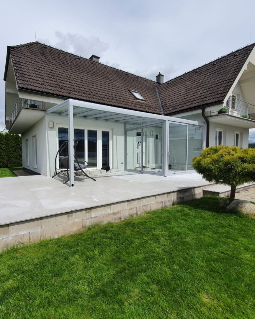 A modern aluminum sunroom with sliding glass walls, built next to a single-family home with a terrace.