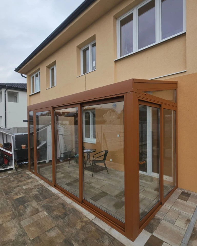 A modern, glass-enclosed addition to a single-family home featuring a brown frame and sliding doors.