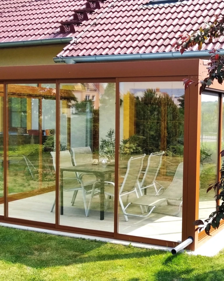 A glass-enclosed aluminum sunroom with a brown frame and garden furniture in Nitra.