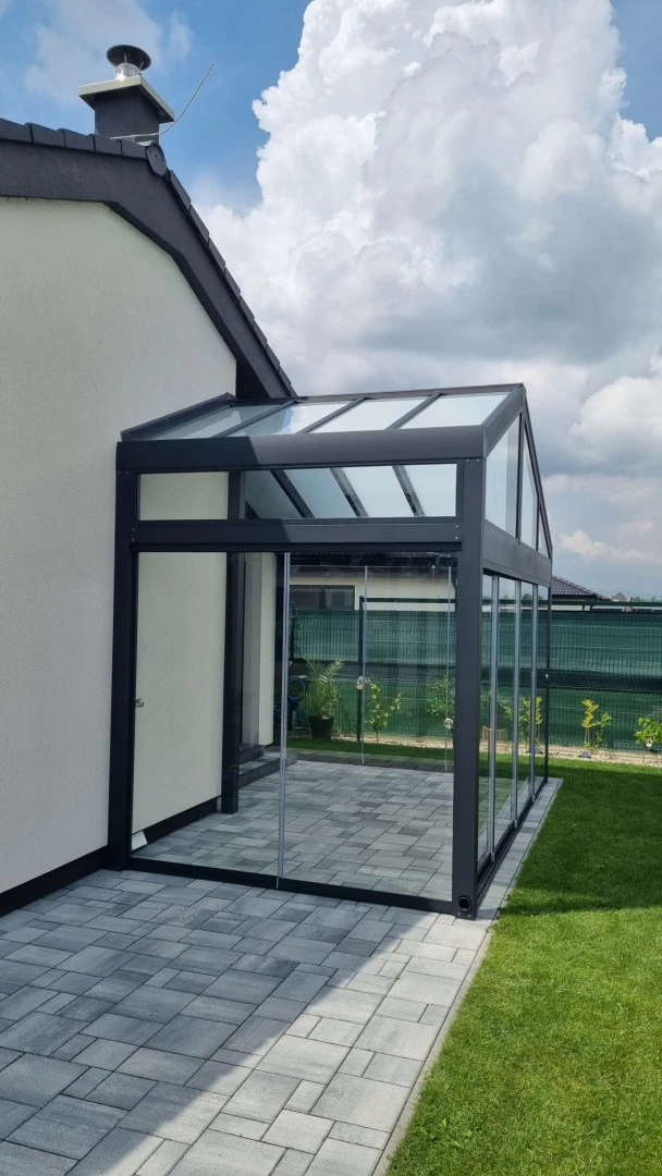 A modern, glass-enclosed sunroom with an anthracite aluminum frame attached to a single-family home
