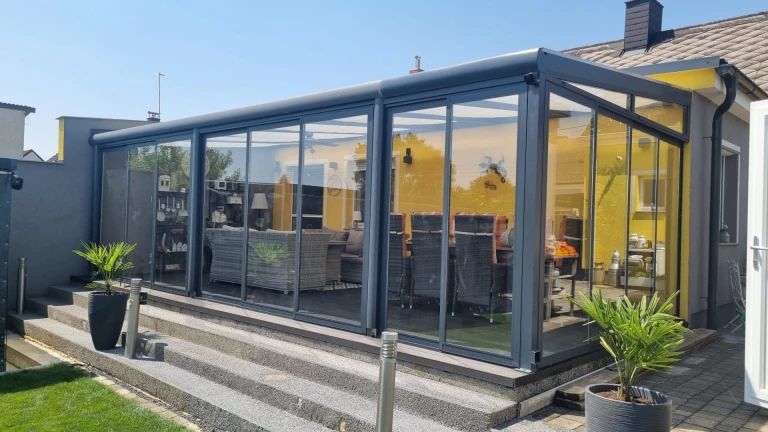 A modern, glass-enclosed aluminum sunroom in anthracite with sliding doors on the house's patio.