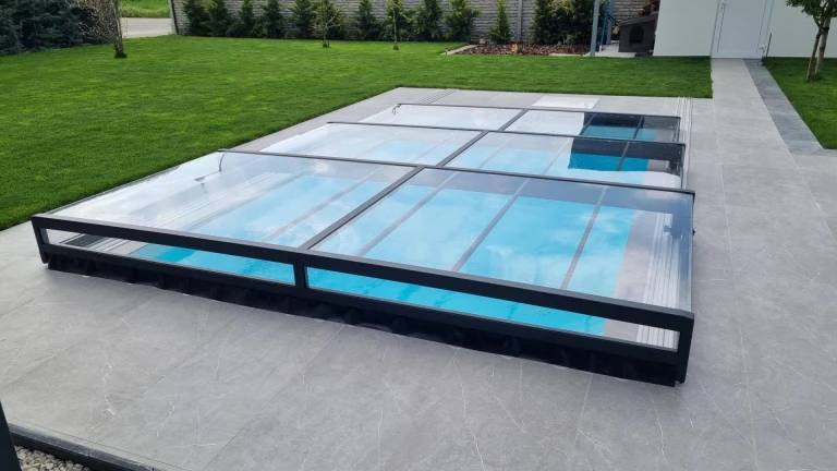 A modern, low-profile aluminum pool enclosure with an anthracite frame and clear glass in the garden