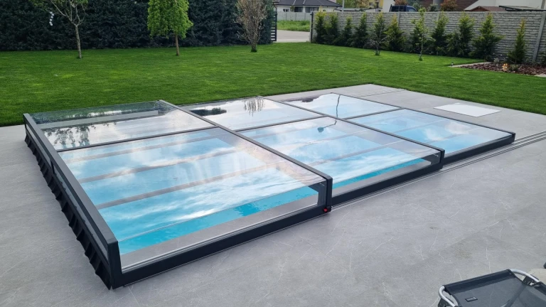 A modern, low-profile aluminum pool enclosure with a transparent panel in the garden