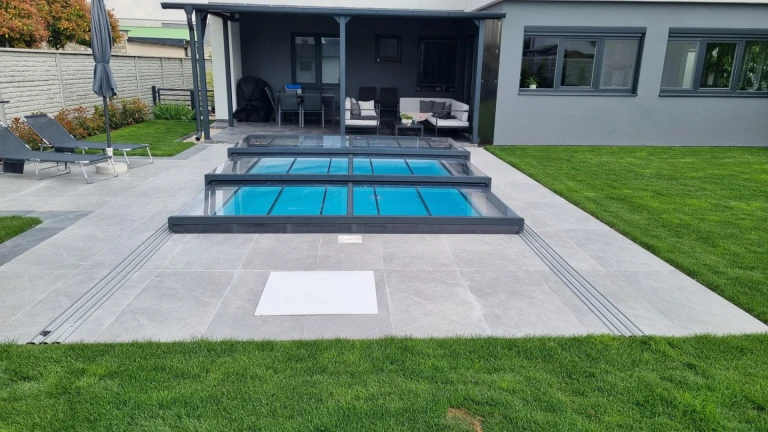 A modern, low-profile aluminum pool enclosure in anthracite on the terrace of a single-family home