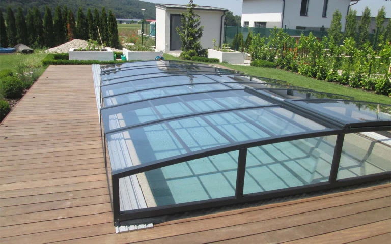 A modern, low-profile aluminum pool enclosure in a dark color on a wooden deck