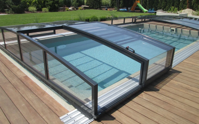 A modern, anthracite-colored low-profile pool enclosure on a wooden deck in the garden