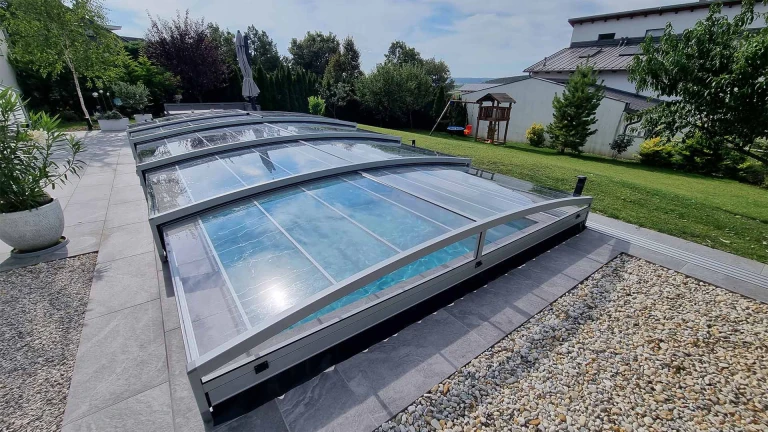 A modern, low-profile pool enclosure with a transparent panel in the garden of a single-family home