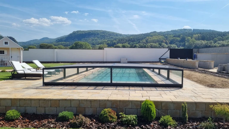 A modern, low-profile aluminum pool enclosure in a garden overlooking the hills