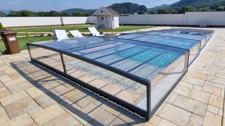 A modern, low-profile glass pool enclosure on a tiled terrace with a view of the hills