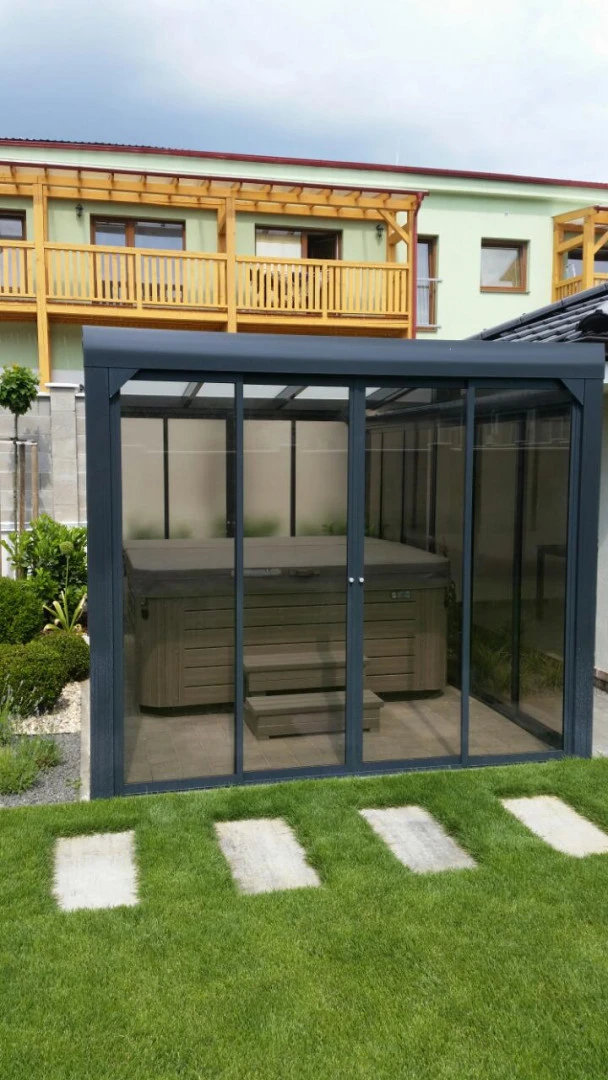A modern glass-enclosed shelter with a hot tub located in the garden of a single-family home.