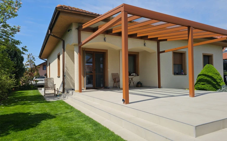 A modern brown aluminum pergola with a glass roof on the paved patio of a single-family home