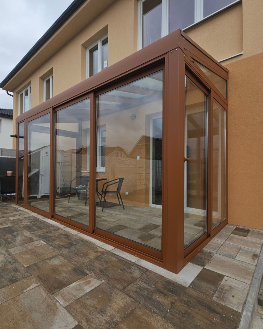 A modern, glass-enclosed conservatory with a brown frame attached to a single-family home.