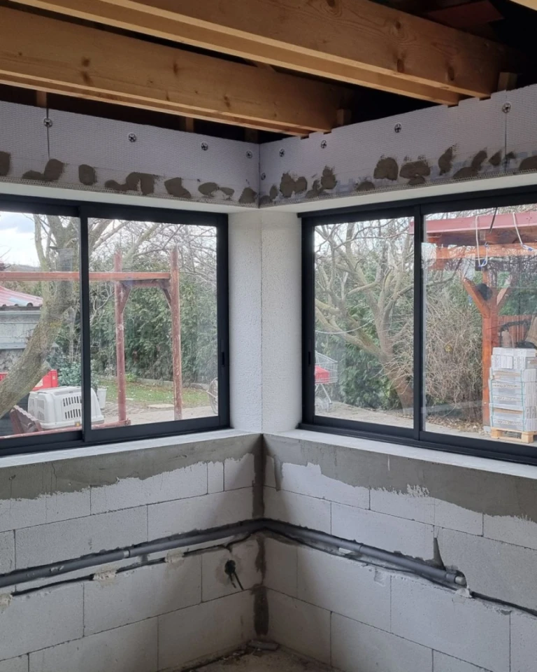 A close-up view of the installation of sliding windows on a terrace under construction with gray frames.