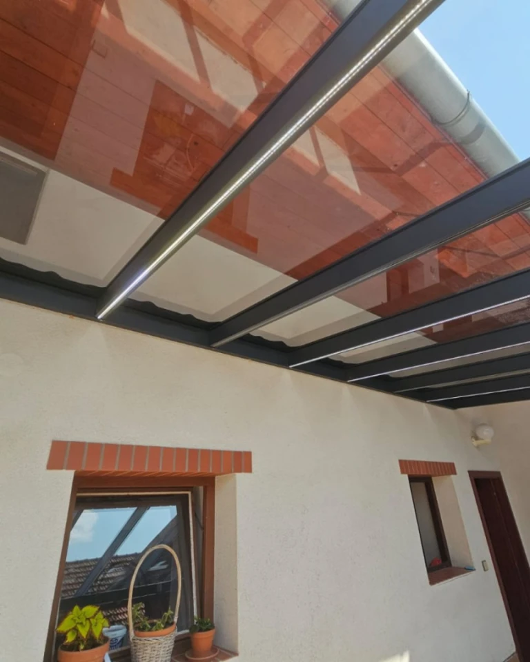 A close-up view of the roof of an aluminum pergola with integrated LED lighting attached to the house's facade.