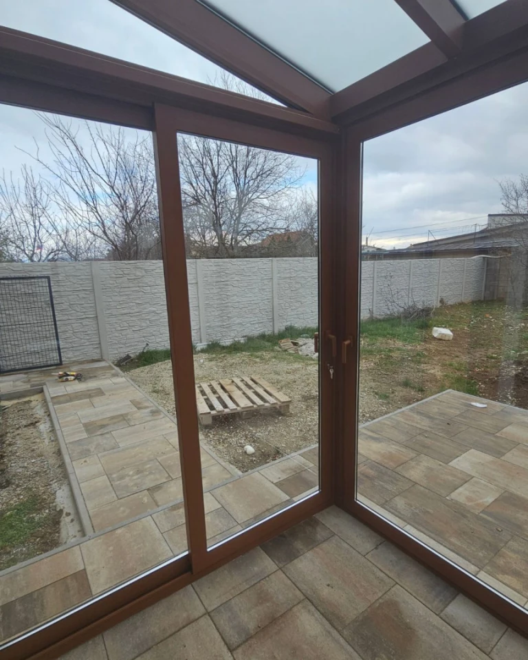 A detailed interior view of a glass-enclosed sunroom with a brown frame and a view of the backyard.