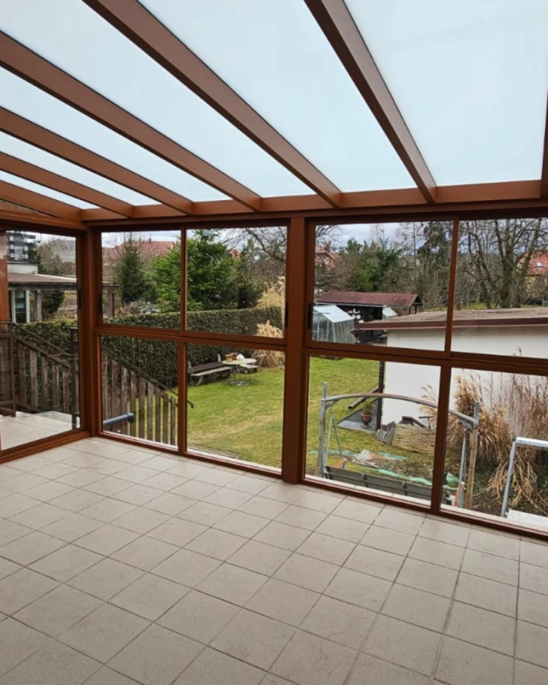 A view from inside a brown, glass-enclosed aluminum pergola overlooking the garden