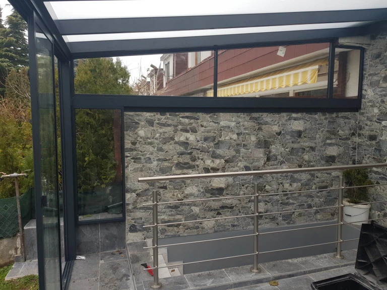 A modern sunroom with an anthracite aluminum frame and stone wall cladding.