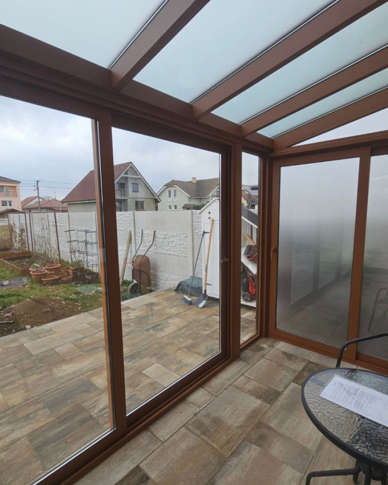 A view from inside the glass-enclosed shelter with a brown frame out onto the yard and the surrounding houses
