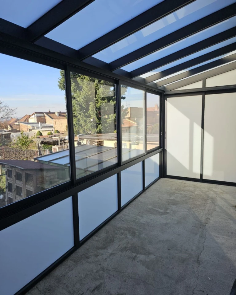 The interior of a glass-enclosed aluminum structure with a view of the surrounding houses and gardens.