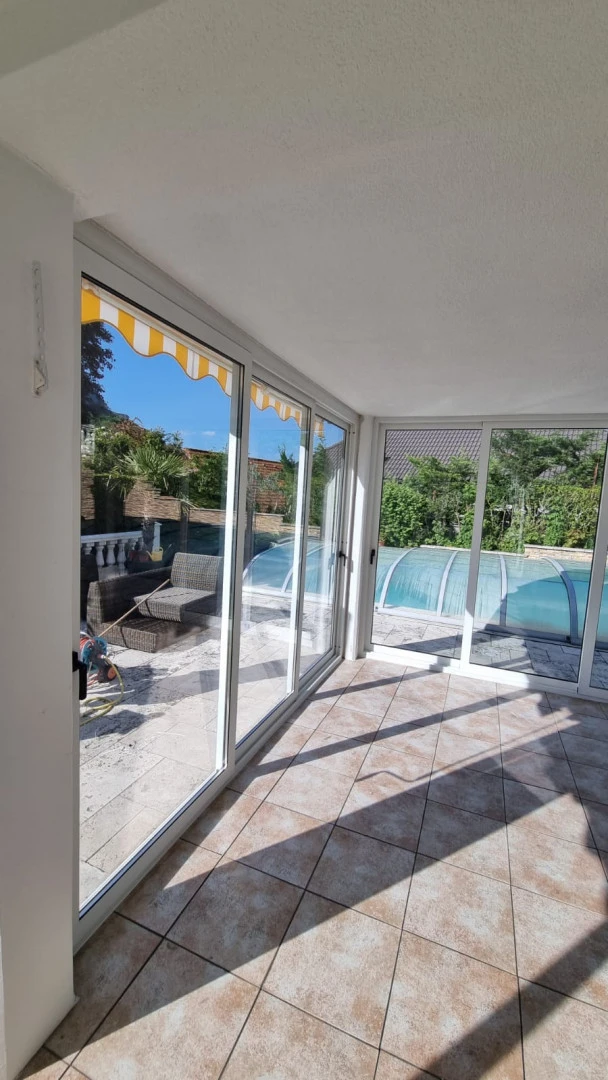 A view from inside the house of the glass-enclosed terrace overlooking the pool and garden.