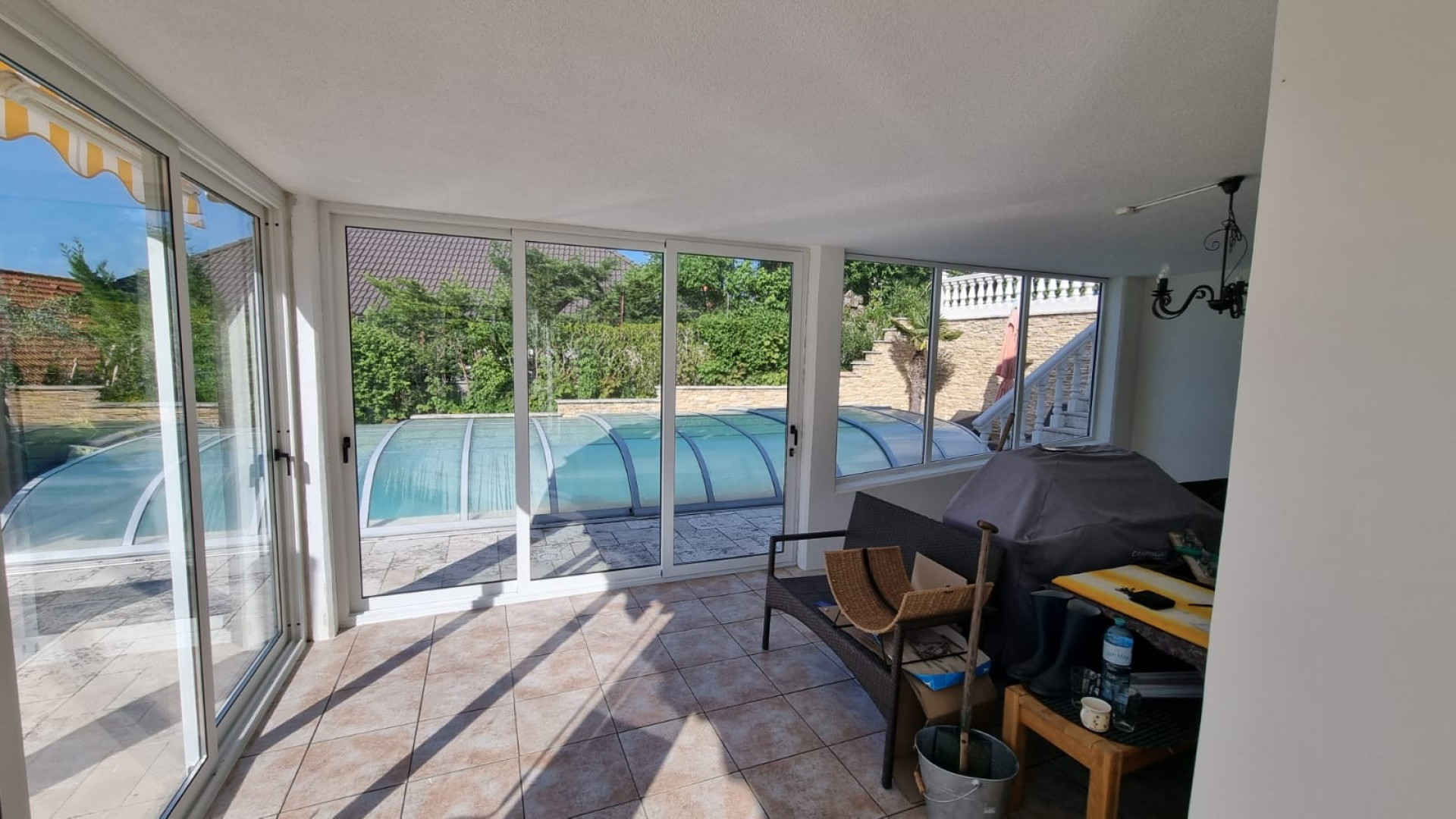 A glass-enclosed terrace with white frames and a view of the pool in the garden