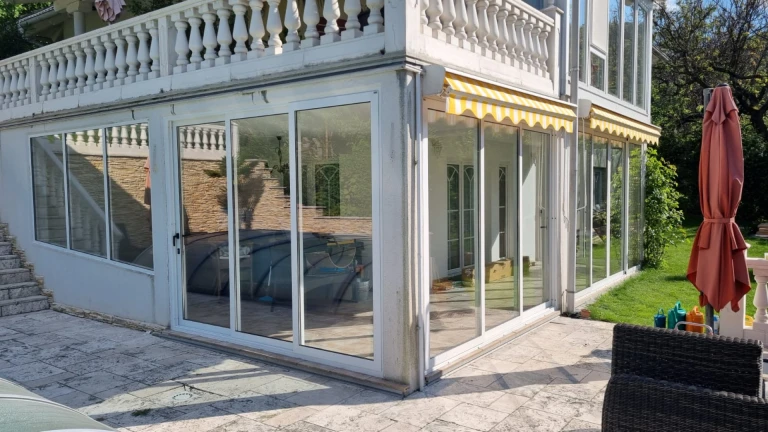 A modern glass enclosure for the lower part of the terrace with white frames and an awning